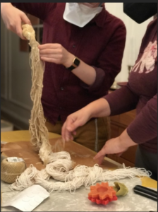 one person holds a thick bunch of very long wick which is sitting on the table, and another person is reaching for the ends